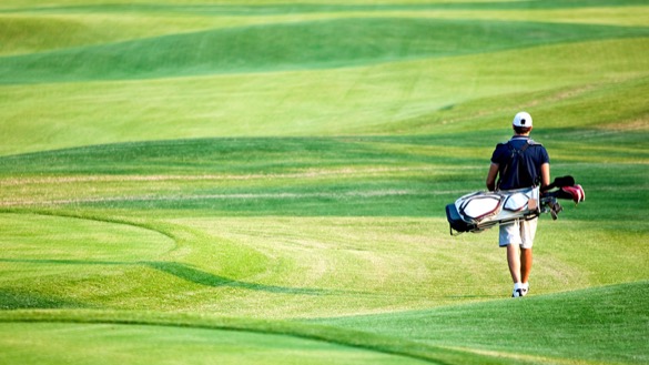 Mann von hinten mit Golfbag laufend über Green.